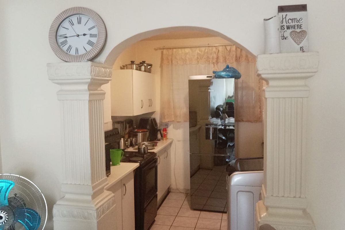 A compact kitchen featuring white cabinetry, tiled flooring, and a functional layout, accessed through a decorative arched entryway.