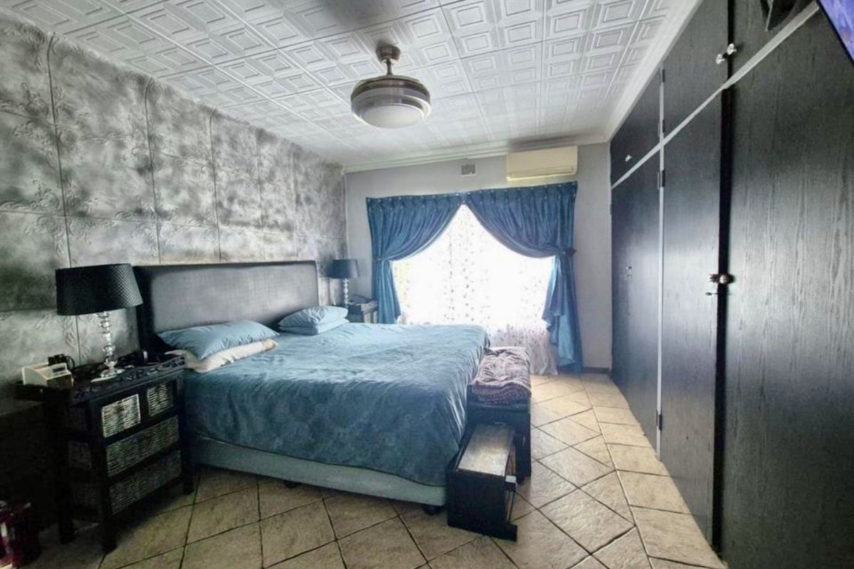 A bedroom featuring tiled flooring, built-in floor-to-ceiling wardrobes, a textured feature wall, and a wall-mounted air conditioning unit.