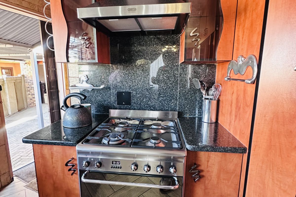 A kitchen cooking station featuring a stainless steel gas stove, extractor fan, granite countertops, and wooden cabinetry.