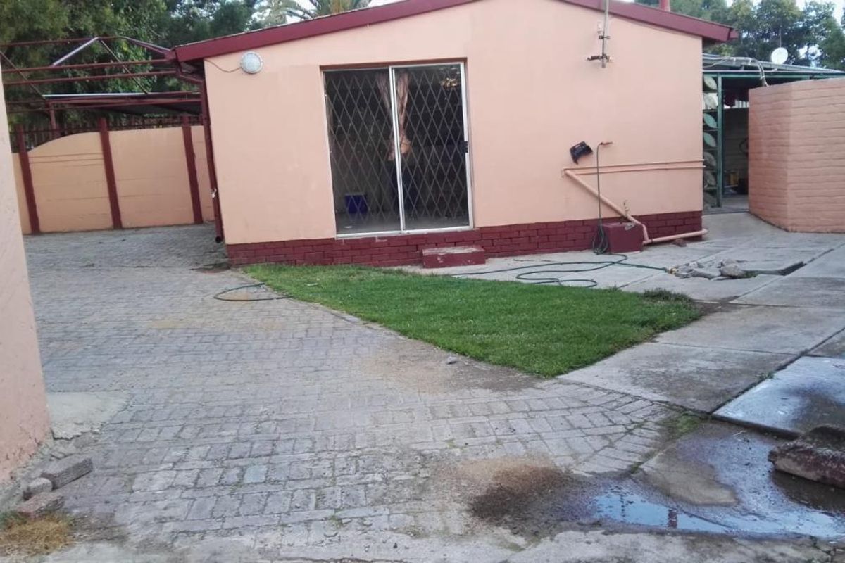 Rear exterior view of the property featuring paved driveway, small lawn area, and sliding glass door access to the main building structure.