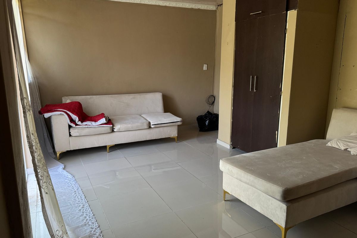 A living area featuring tiled flooring and a built-in wardrobe, showing signs of wear and requiring cosmetic updates.