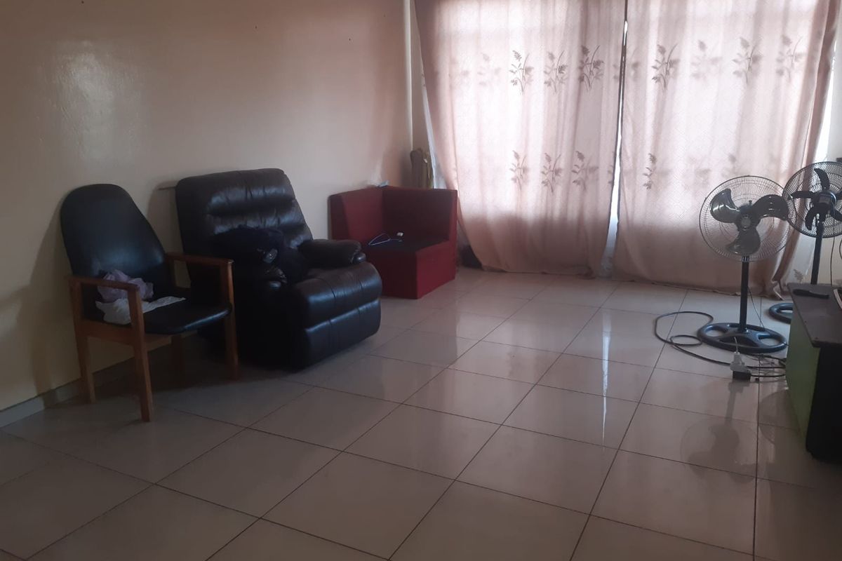A living room area featuring tiled flooring and large window coverage, providing a functional space with potential for cosmetic updates.