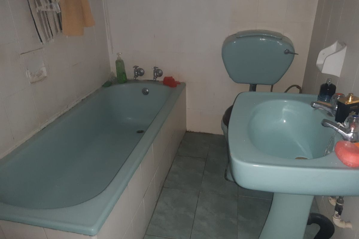 A dated bathroom featuring a vintage blue bathtub, matching pedestal basin, and toilet, with tiled flooring and wall finishes.