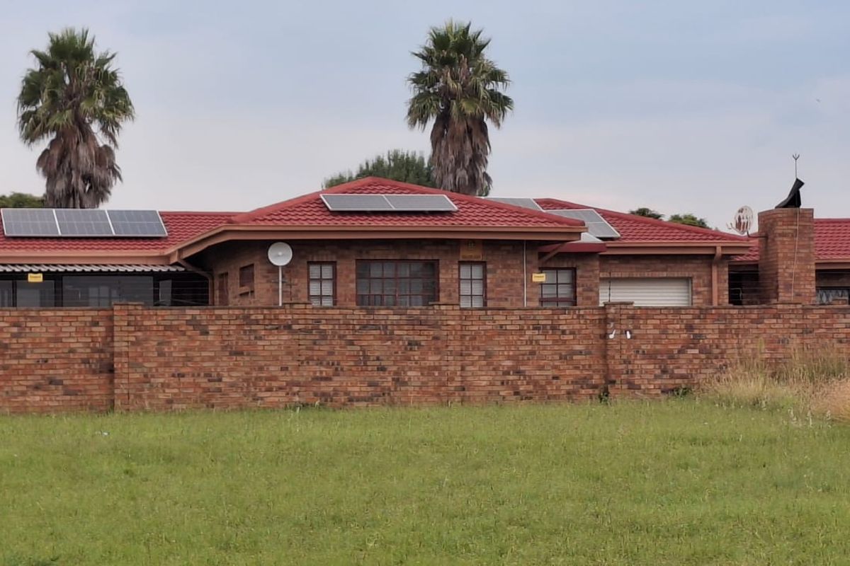Exterior view of a brick townhouse featuring a red tiled roof, solar panels, and a perimeter boundary wall.