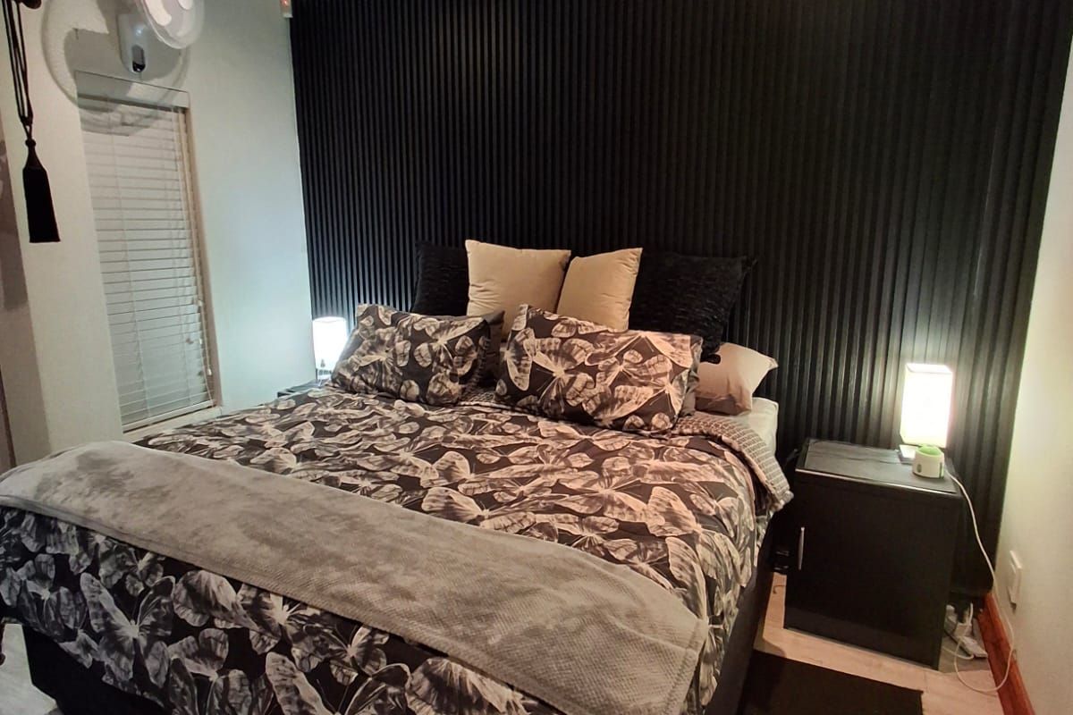 A well-maintained bedroom featuring a modern black vertical slat feature wall, light wood-look flooring, and recessed ceiling lighting.