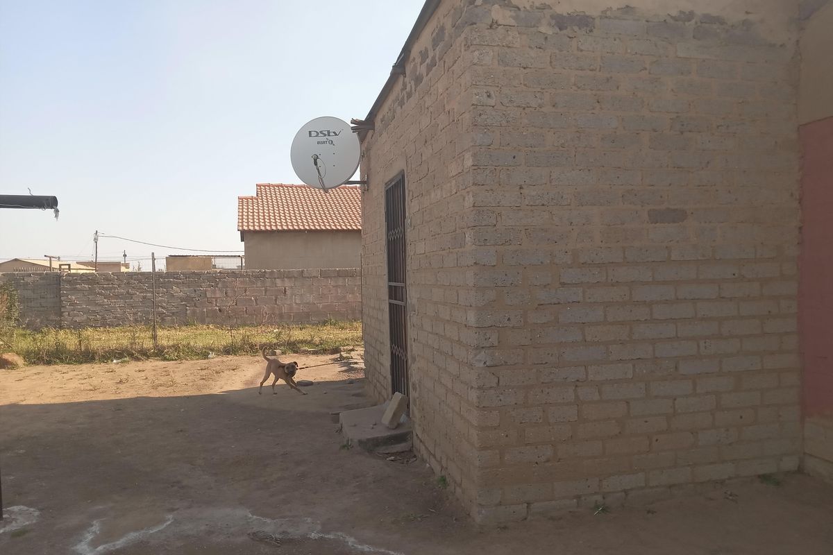 Exterior view of a residential property featuring exposed brick walls, a security gate, and a satellite dish mounted on the side.