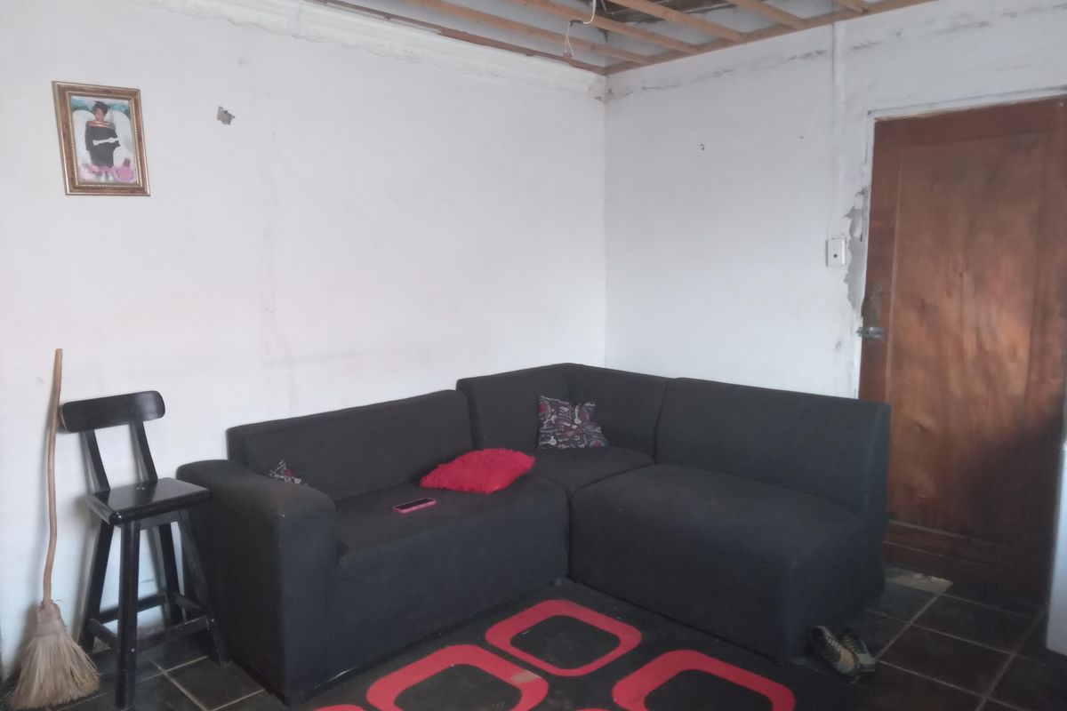 A living room area featuring tiled flooring and an unfinished ceiling with exposed timber joists, requiring renovation and ceiling installation.