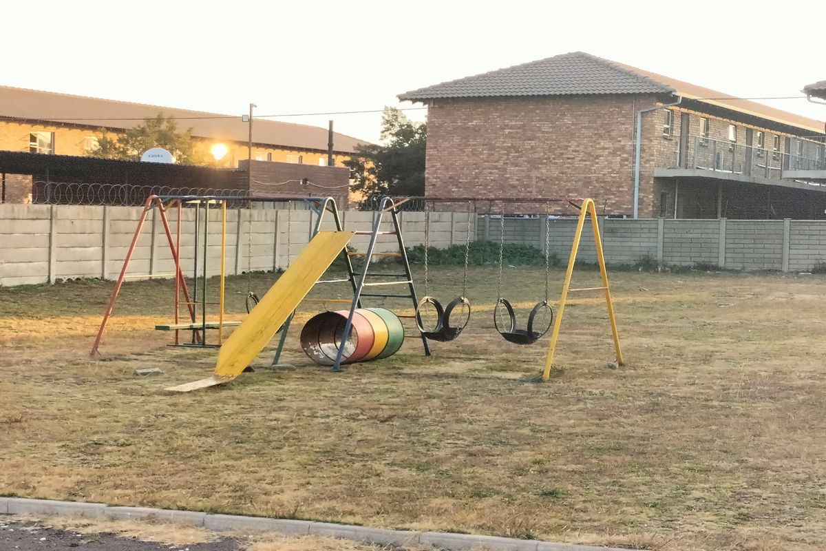 Communal outdoor area featuring a playground with swings and a slide, set within a residential apartment complex.
