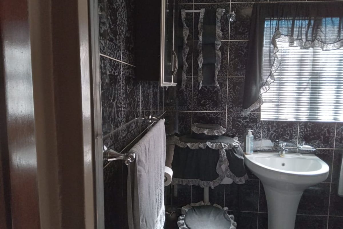A compact bathroom featuring dark patterned wall tiles, a white pedestal basin, and a standard toilet.