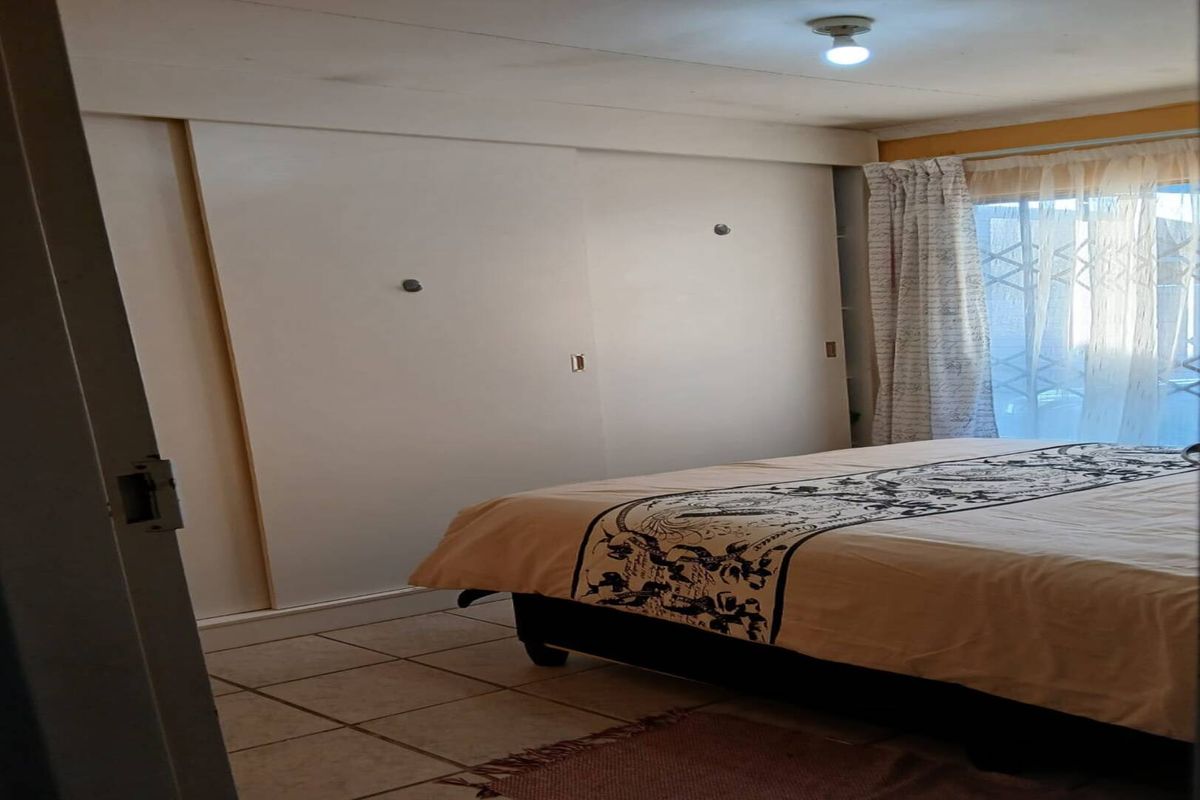 A bedroom featuring built-in sliding door cupboards, tiled flooring, and a window with curtain treatments.