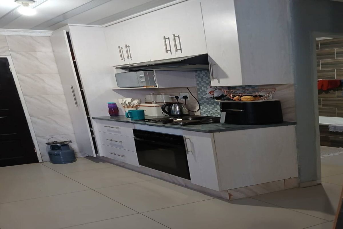 A compact kitchen featuring white cabinetry, a built-in oven, a gas hob with an extractor fan, and tiled flooring.