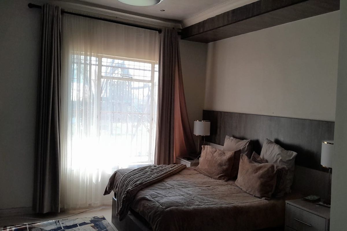 A bedroom featuring a built-in headboard with integrated side tables and a large window with security bars.