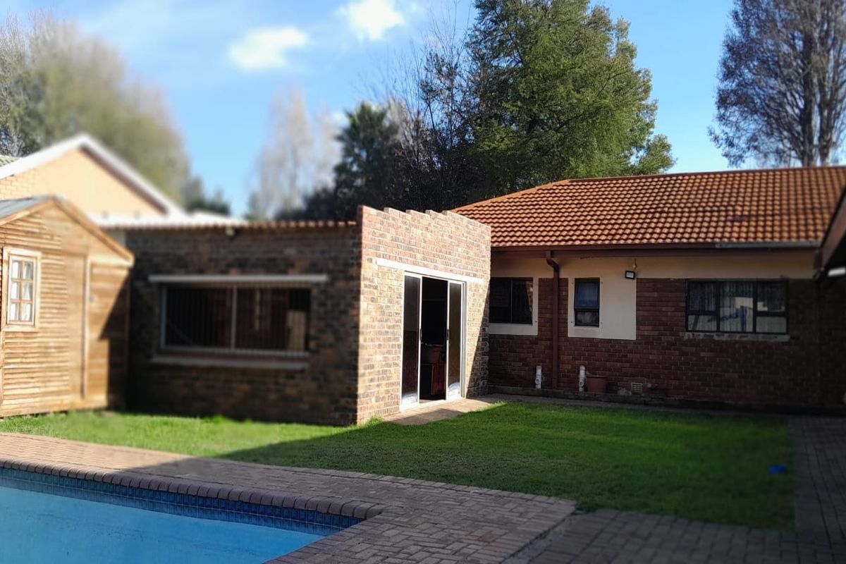 Rear exterior view of the property featuring a swimming pool, brick facade, and a small wooden outbuilding set within a garden area.
