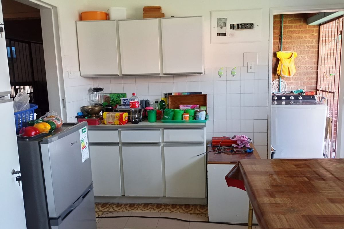 A functional kitchen area featuring white cabinetry, tiled splashbacks, and tiled flooring, with an adjacent utility space visible through the doorway.