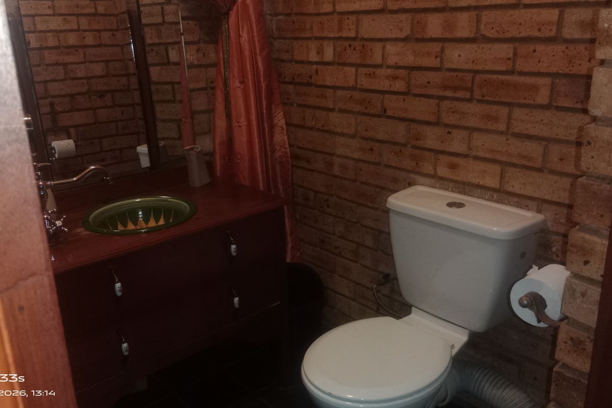 A compact bathroom featuring exposed brick walls, a vanity with a decorative basin, and a standard toilet.