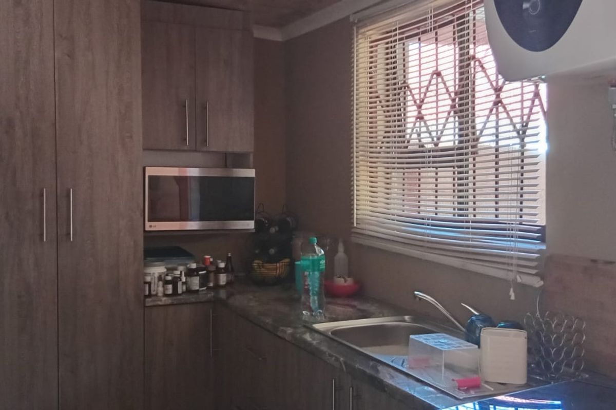 A functional kitchen featuring wood-look cabinetry, a stainless steel sink, built-in microwave, and a wall-mounted electric water heater.
