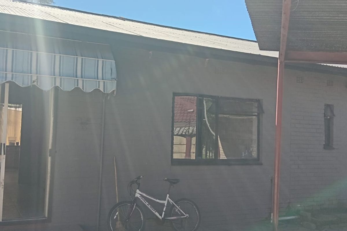 Rear exterior view of the house featuring a covered patio area, brick facade, and metal roofing with integrated security gates and windows.