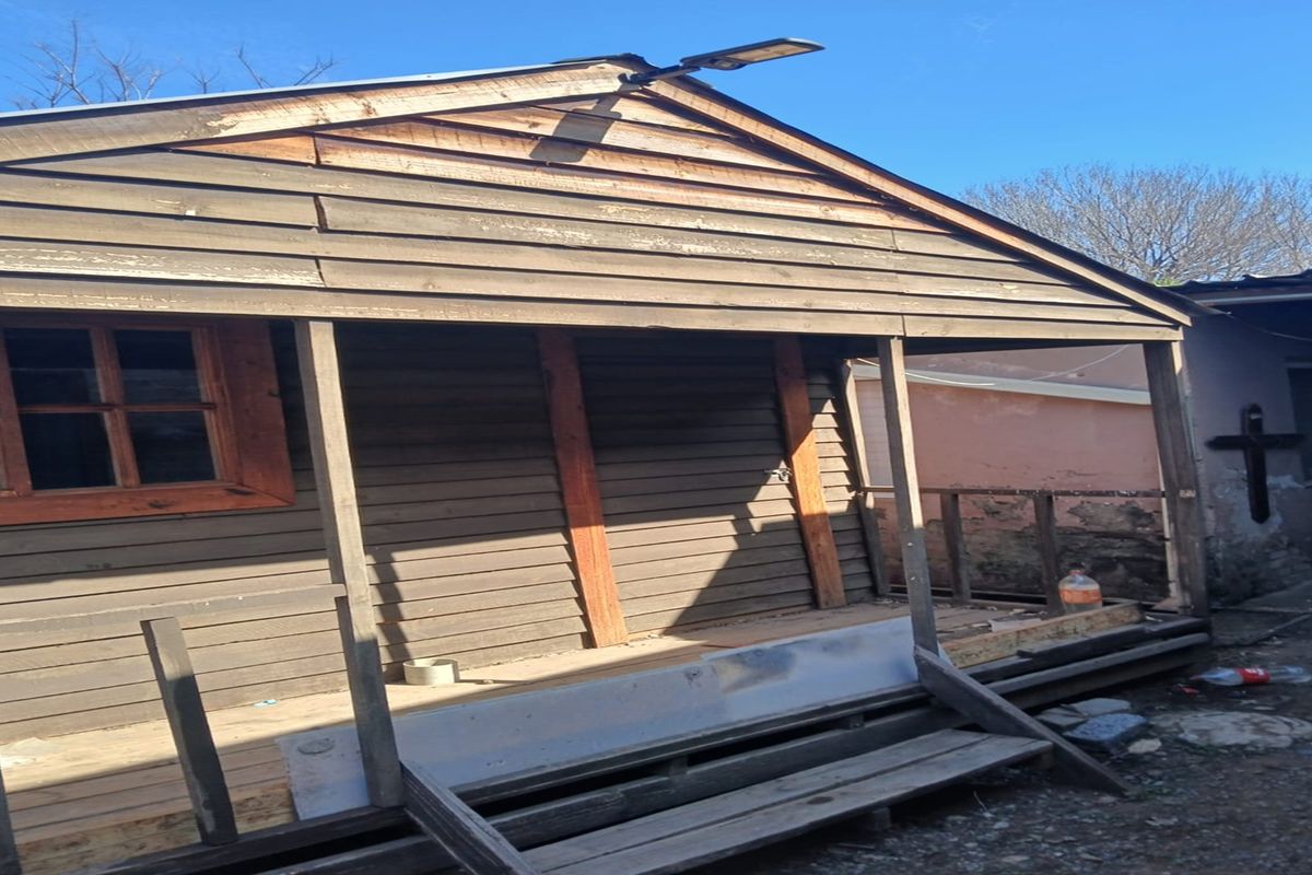 Exterior view of a weathered timber-clad structure featuring a front porch area, showing signs of significant wear and requiring maintenance.