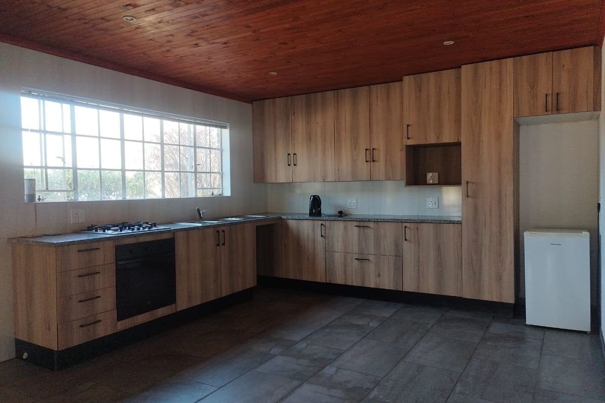 A functional kitchen featuring modern wood-look cabinetry, granite countertops, a built-in oven and gas hob, tiled flooring, and a warm timber-paneled ceiling.