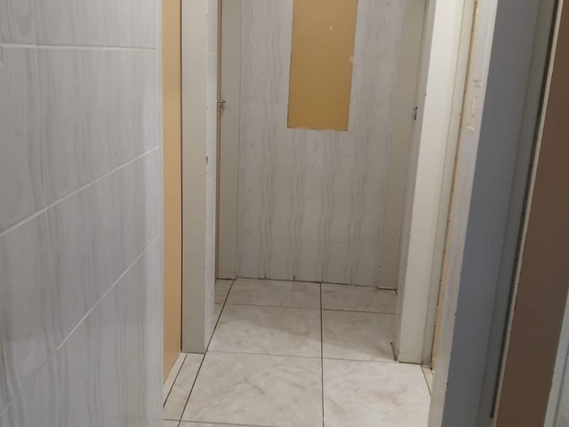 A narrow hallway featuring ceramic wall and floor tiles, currently showing an unfinished wall section requiring repair.