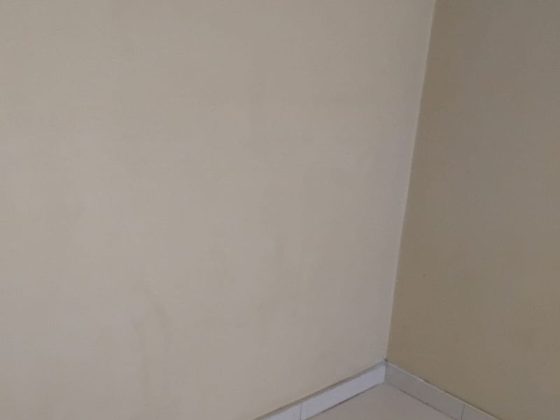 A corner view of an empty room featuring neutral wall paint and light-colored floor tiles with matching skirting boards.