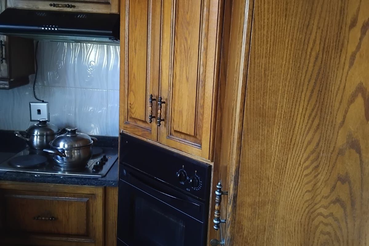 A functional kitchen featuring traditional wooden cabinetry, a built-in oven, a hob with an extractor fan, and a tiled backsplash.
