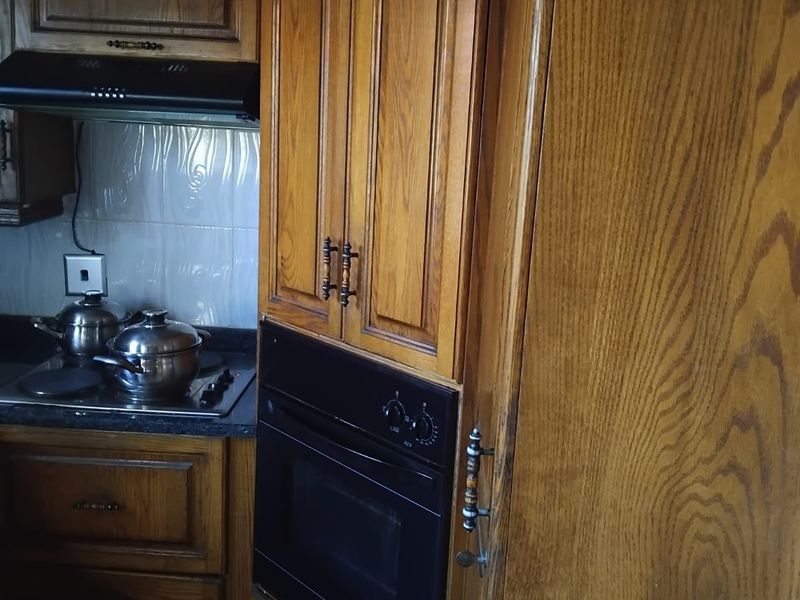 A functional kitchen featuring traditional wooden cabinetry, a built-in oven, a hob with an extractor fan, and a tiled backsplash.
