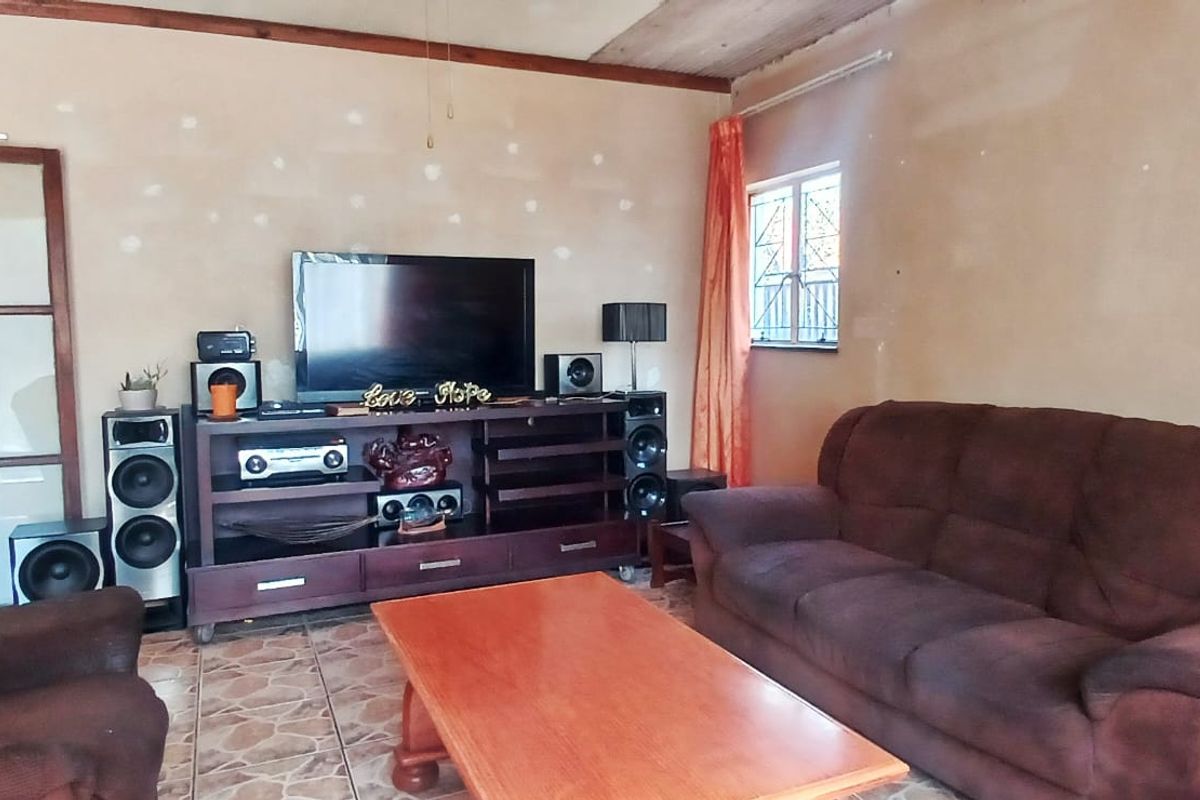 A living room featuring tiled flooring, a sliding glass door, and security bars on the window, currently requiring cosmetic wall and ceiling finishing.