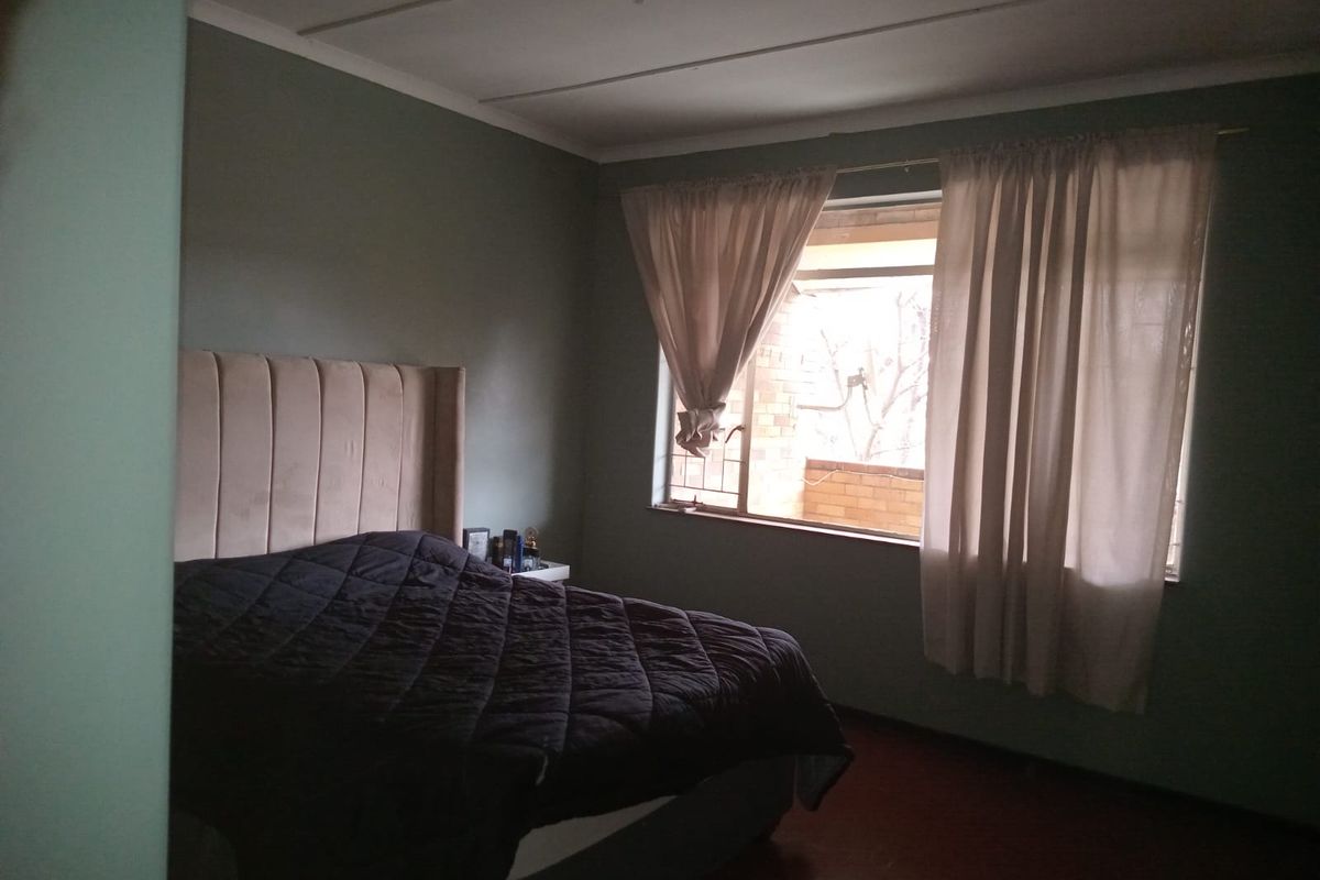 A bedroom featuring a window with security bars and curtains, providing natural light and a view of the exterior brickwork.