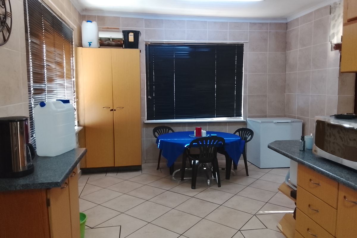 A functional kitchen area featuring tiled flooring, built-in wooden cabinetry, and ample space for a dining table.