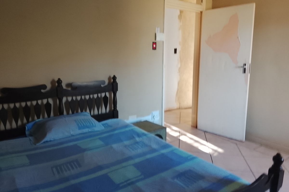 A bedroom featuring tiled flooring and a doorway leading to an adjacent space with visible wall plaster damage.