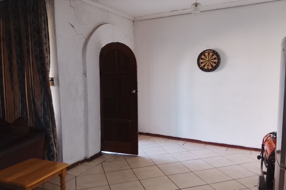 A living area featuring tiled flooring and a distinctive arched wooden doorway, showing signs of wear and structural cracking in the walls and ceiling.