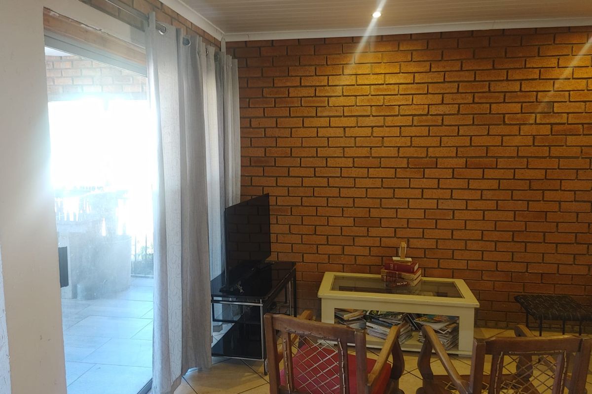 A living room featuring exposed brick walls, tiled flooring, and large sliding glass doors providing access to an outdoor patio area.
