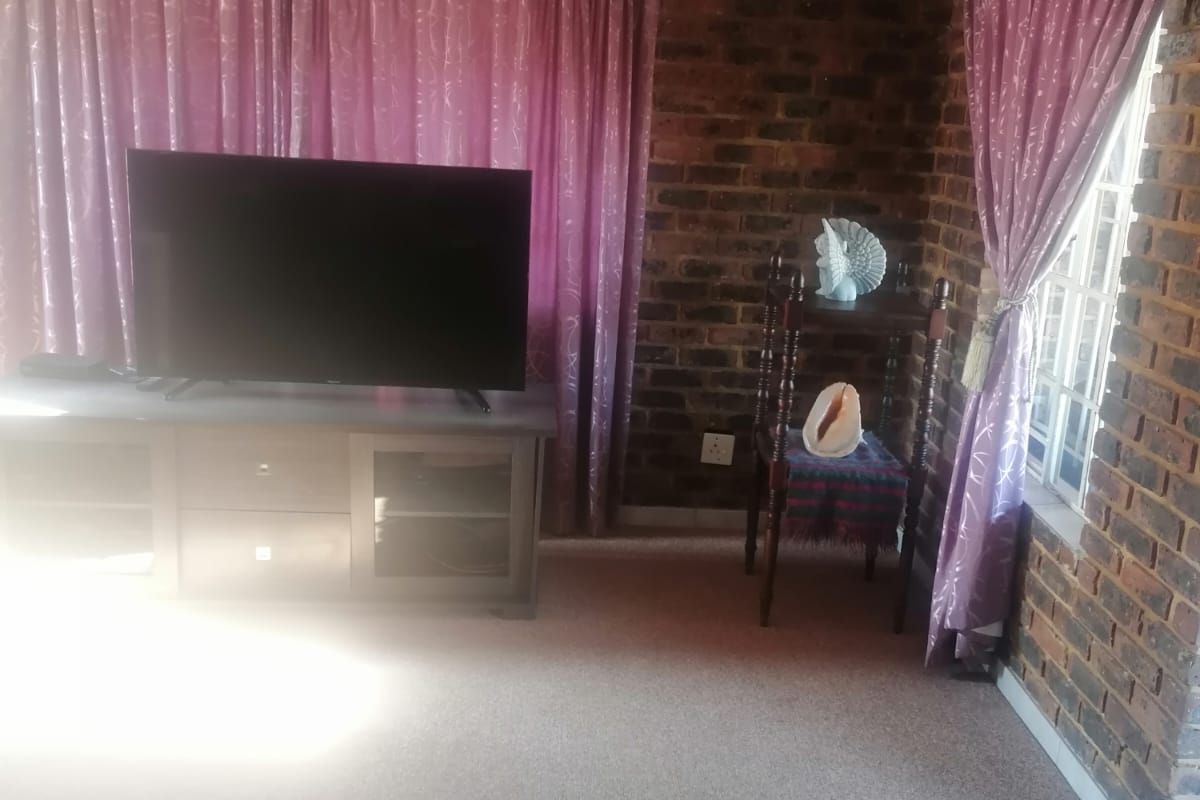 A living room featuring exposed face-brick walls, carpeted flooring, and large windows with curtains, providing a rustic and textured aesthetic.