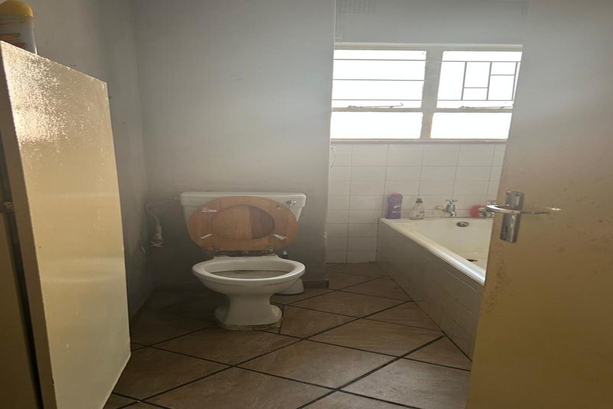 A dated bathroom featuring a standard bathtub, toilet, and tiled flooring, requiring cosmetic updates to modernize the space.