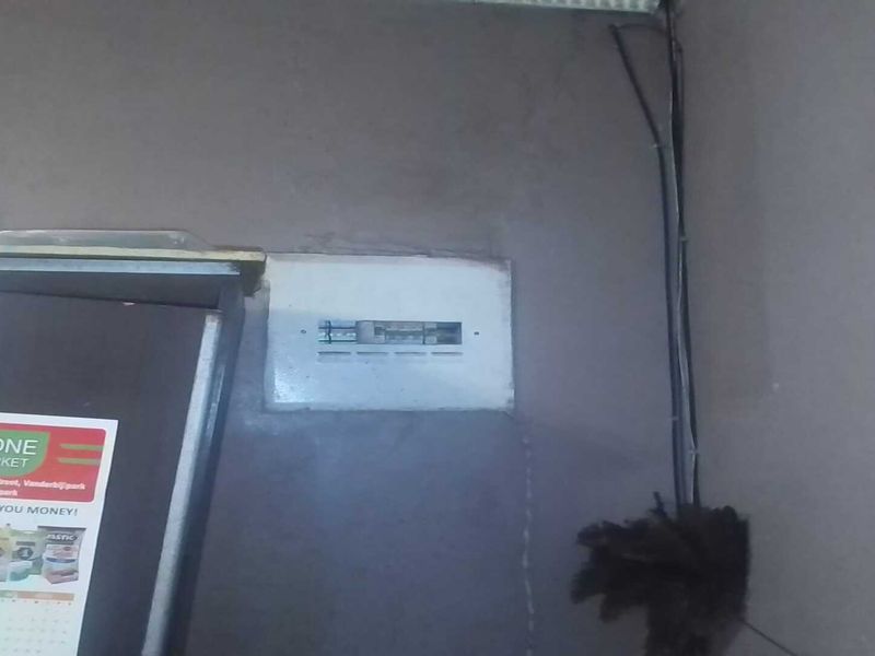 A utility area featuring an exposed electrical distribution board and visible wiring on a damaged wall surface.