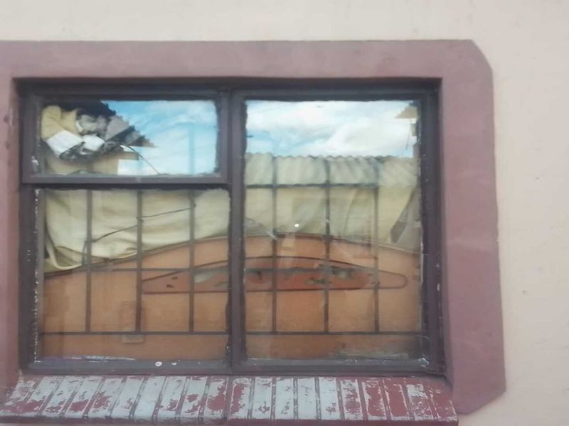 A close-up view of a residential window featuring security bars, showing signs of wear and damage to the frame and sill.