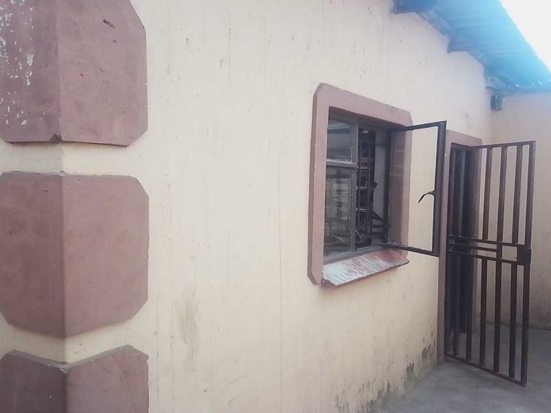 Exterior view of the rear building facade featuring security gates, burglar bars, and concrete paving, showing signs of wear and maintenance requirements.