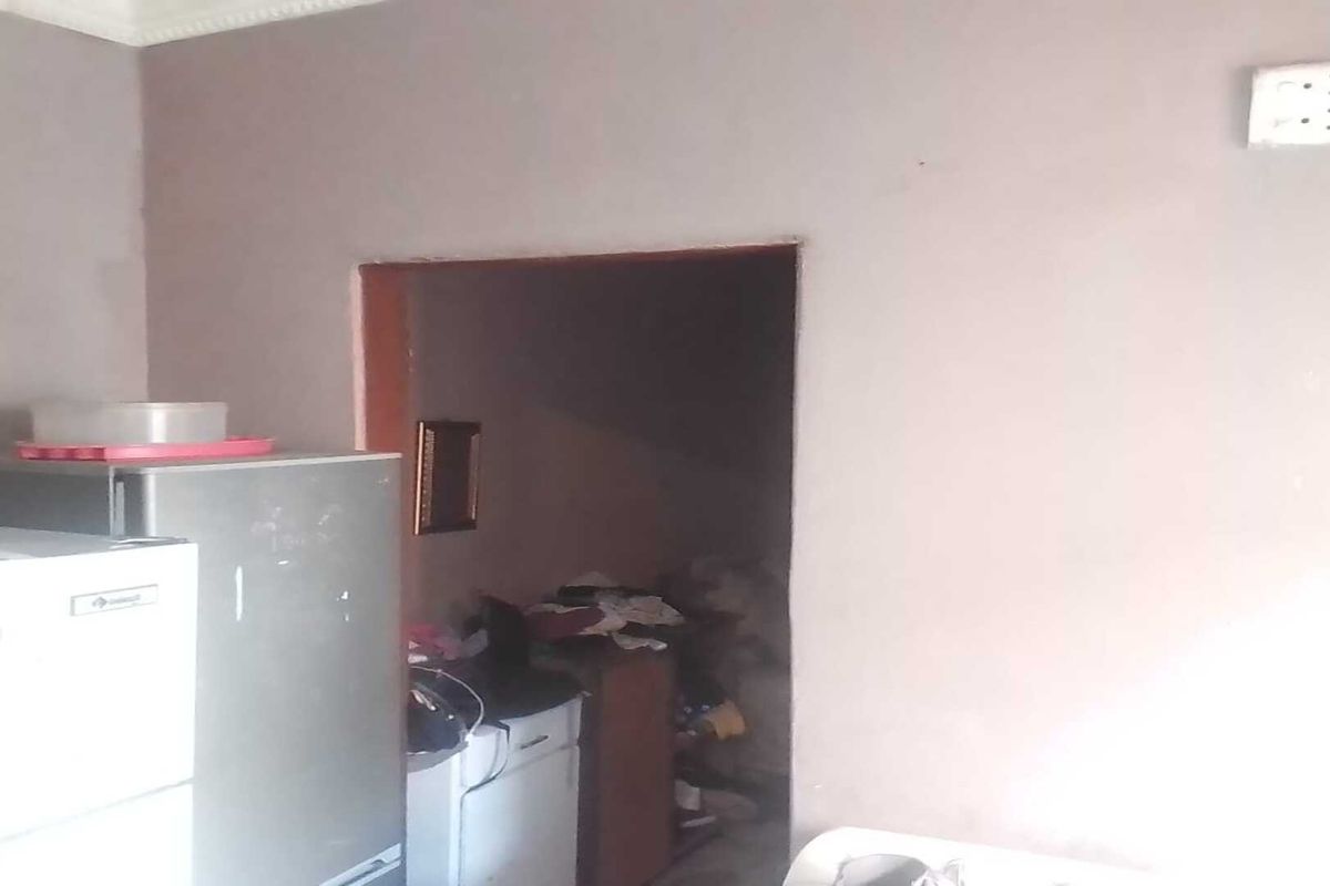 A basic kitchen area featuring plain walls and an electrical outlet, requiring cosmetic updates and improved lighting to enhance the space.