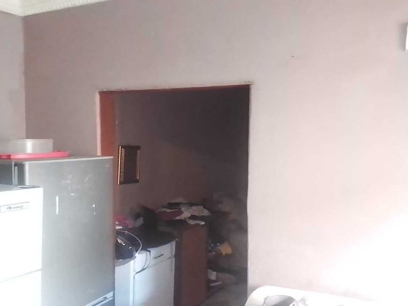 A basic kitchen area featuring plain walls and an electrical outlet, requiring cosmetic updates and improved lighting to enhance the space.