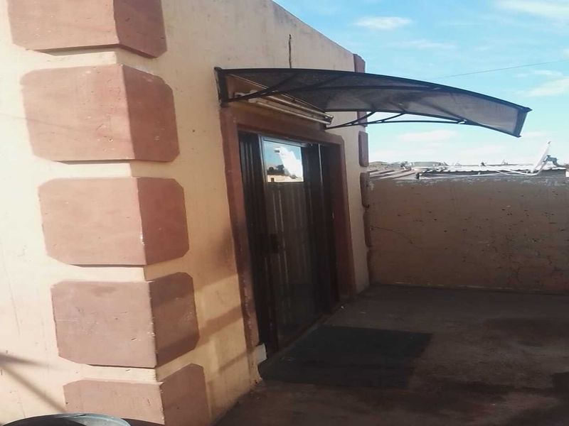 A rear exterior view showing a sliding glass door entrance with a protective polycarbonate awning and a concrete patio area.