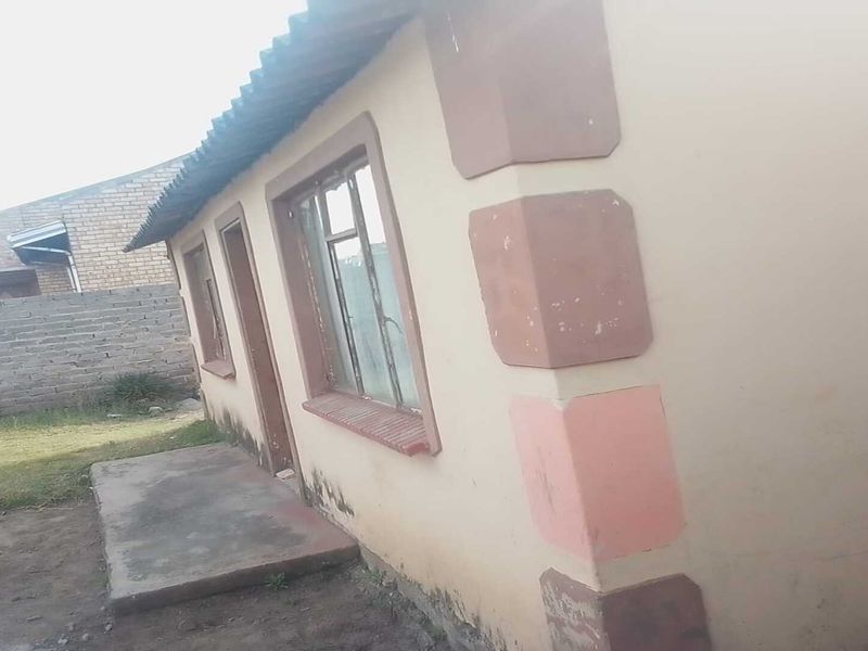 Rear exterior view of a single-story house featuring a concrete patio, metal window frames, and visible signs of exterior wall weathering and damp.