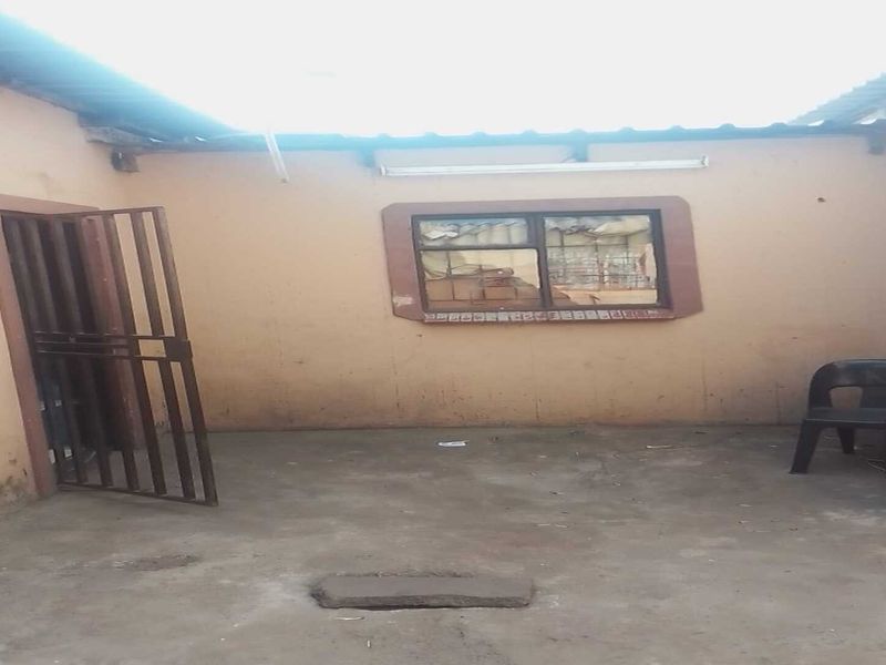 An outdoor patio area featuring concrete flooring, a security gate, and a window, requiring maintenance and cosmetic updates to improve its overall condition.