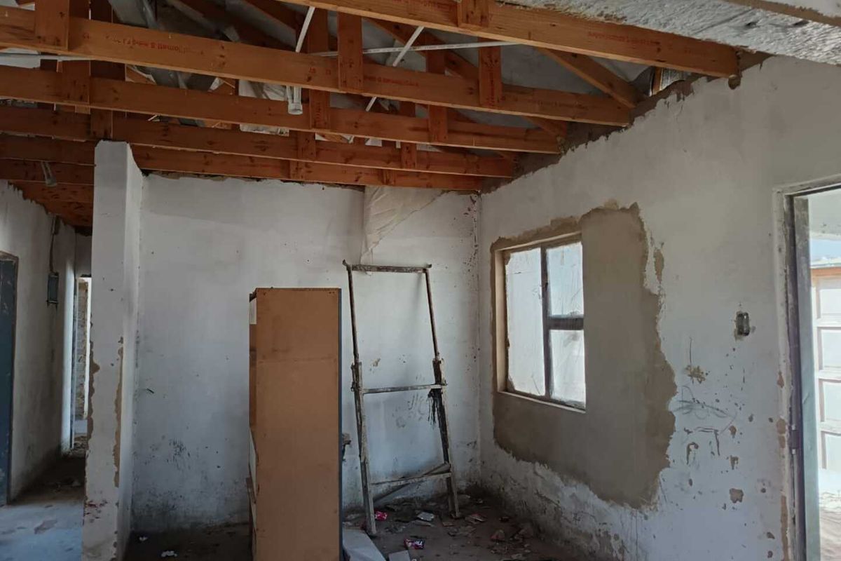 An interior room currently under renovation, featuring exposed timber roof trusses, unfinished plastered walls, and a basic window frame.
