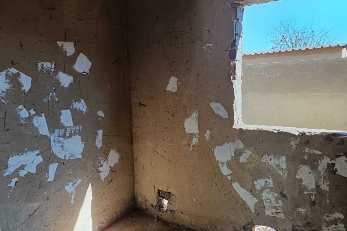 An interior room in shell condition featuring unfinished plaster walls and an exposed window opening, requiring significant renovation and finishing work.