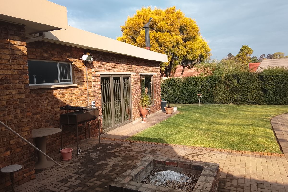 A spacious rear garden featuring a brick-paved patio area with a built-in fire pit, overlooking a well-maintained lawn and established hedge boundary.