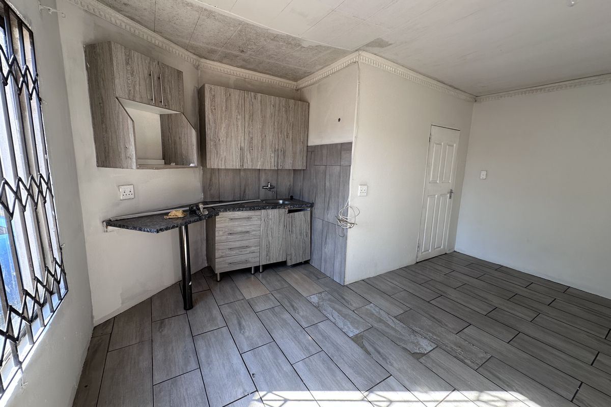 Compact kitchen area featuring wood-look cabinetry, tiled flooring, and a small breakfast bar, requiring some cosmetic attention to the ceiling and finishes.