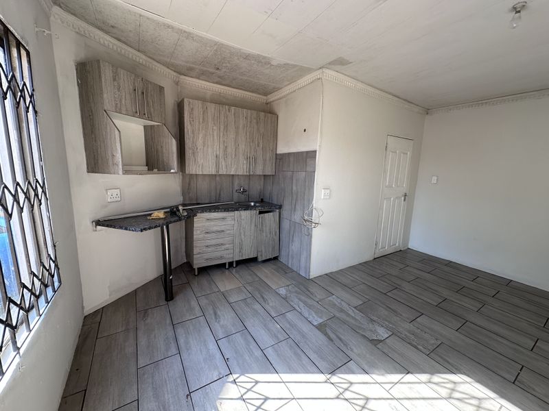 Compact kitchen area featuring wood-look cabinetry, tiled flooring, and a small breakfast bar, requiring some cosmetic attention to the ceiling and finishes.