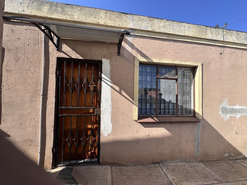 Exterior view of an apartment entrance featuring a security gate, window security bars, and a small protective awning over the doorway.
