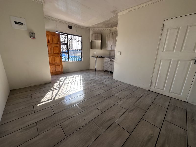 An empty open-plan living and kitchen area featuring wood-look floor tiles, security gates, and basic built-in cabinetry, awaiting personal touches.